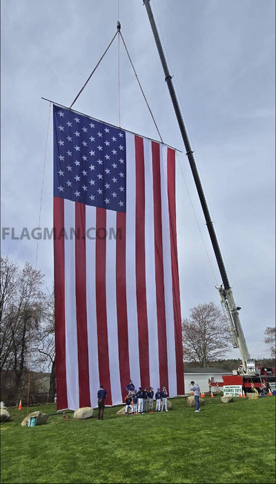 Large American flag being raised with a crane on a grassy field