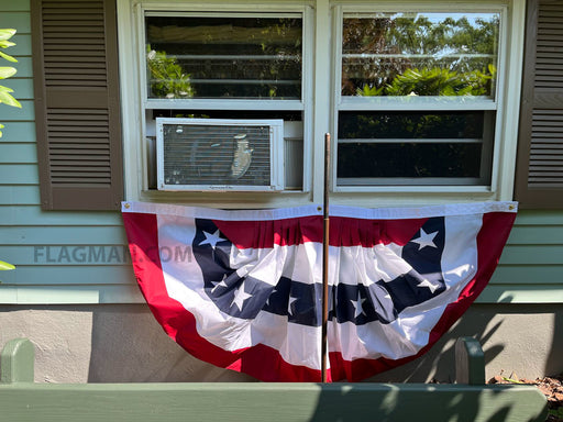 A patriotic bunting banner with red, white, and navy blue stars and stripes hangs in front of a window on a house exterior.