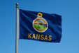 Realistic looking Kansas flag flying on a flagpole with clear blue sunny skies behind it